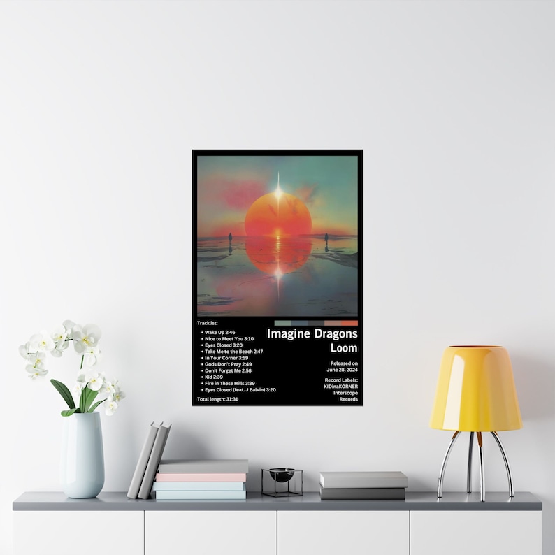 Puede incluir: Una portada de &aacute;lbum en blanco y negro para el &aacute;lbum "Loom" de Imagine Dragons. La portada presenta una puesta de sol sobre una masa de agua con dos figuras caminando en la distancia. El t&iacute;tulo del &aacute;lbum est&aacute; en texto blanco con el nombre de la banda en texto negro. La lista de canciones est&aacute; debajo del t&iacute;tulo del &aacute;lbum.
