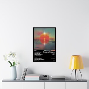 Puede incluir: Un p&oacute;ster para el &aacute;lbum "Loom" de Imagine Dragons. El p&oacute;ster presenta una puesta de sol sobre una masa de agua con un sol rojo y un cielo azul. El t&iacute;tulo del &aacute;lbum est&aacute; en texto blanco con el nombre de la banda en texto negro. La lista de canciones est&aacute; debajo del t&iacute;tulo del &aacute;lbum.
