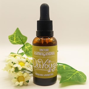 May include: A brown glass bottle with a black dropper, labeled "Tincture Ashwagandha Du Youga Withania Somnifera." The bottle is surrounded by white flowers and green leaves, set against a white background.
