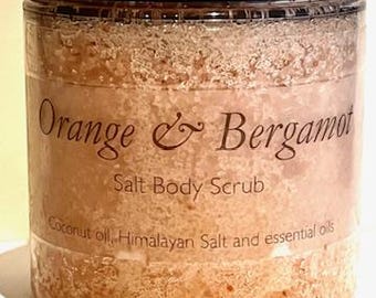 May include: A clear jar with a black lid filled with a light brown salt scrub. The label reads "Orange & Bergamot Salt Body Scrub" and "Coconut oil, Himalayan Salt and essential oils".