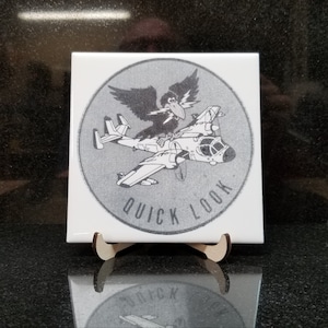 Puede incluir: Un azulejo de cerámica blanco y negro con un gráfico redondo de un cuervo de dibujos animados posado en un avión con las palabras "Quick Look" alrededor del gráfico.