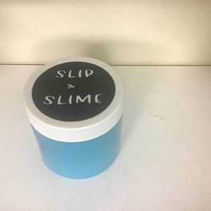 May include: A blue plastic container with a white lid. The lid has a black sticker with the text "SLIP & SLIME" in white.