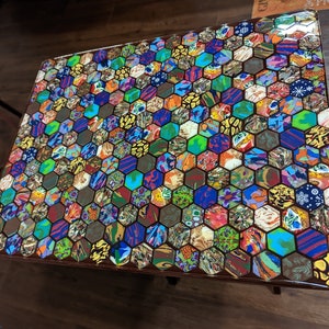 May include: A colorful hexagonal mosaic table top with a glossy finish. The table top is made of many small pieces of colorful material, creating a unique and eye-catching design.