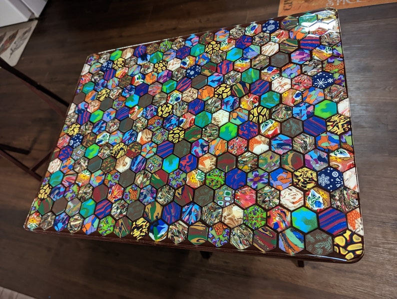 May include: A colorful hexagonal mosaic table top with a glossy finish. The table top is made of many small pieces of colorful material, creating a unique and eye-catching design.