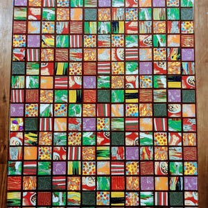 May include: A square table top with a mosaic design. The mosaic is made up of small squares of different colors and patterns, including red, green, yellow, orange, and purple. The table top is made of wood and has a dark brown finish.