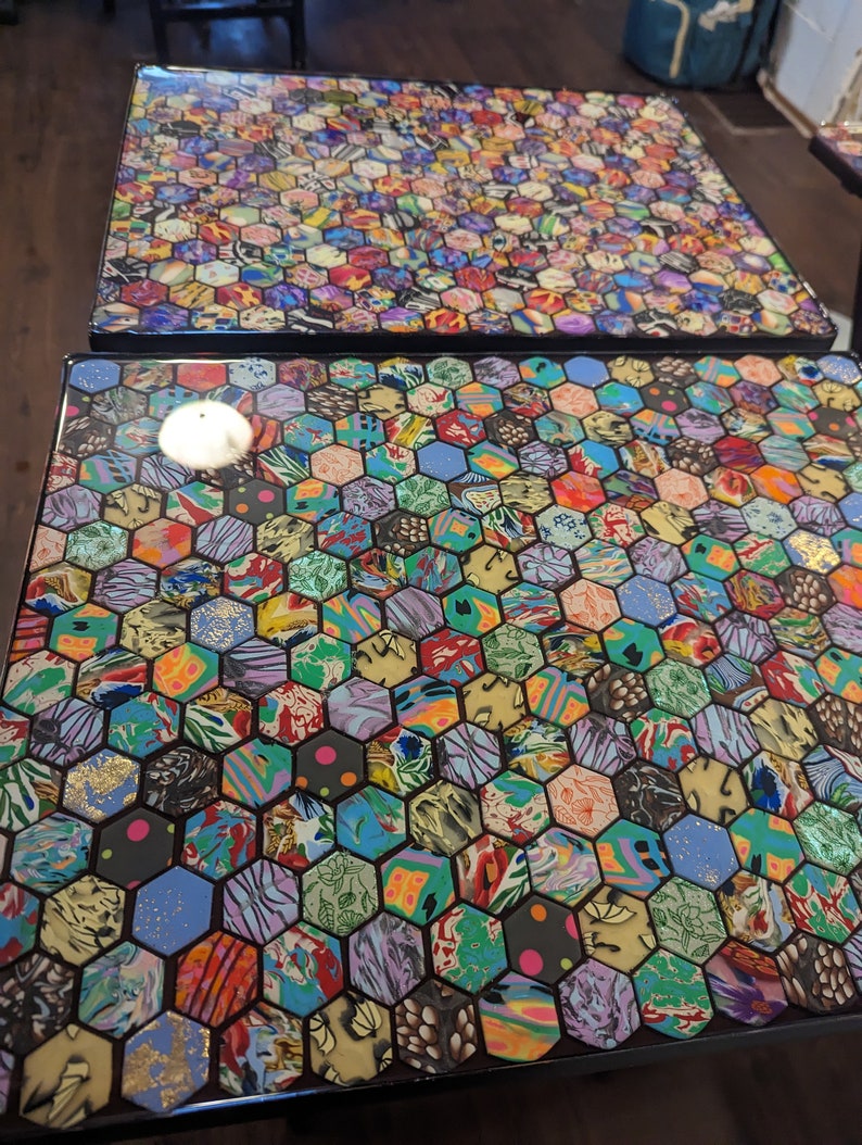 May include: Two square tables with black legs and a hexagonal mosaic top. The mosaic is made of colorful, patterned tiles with gold accents.