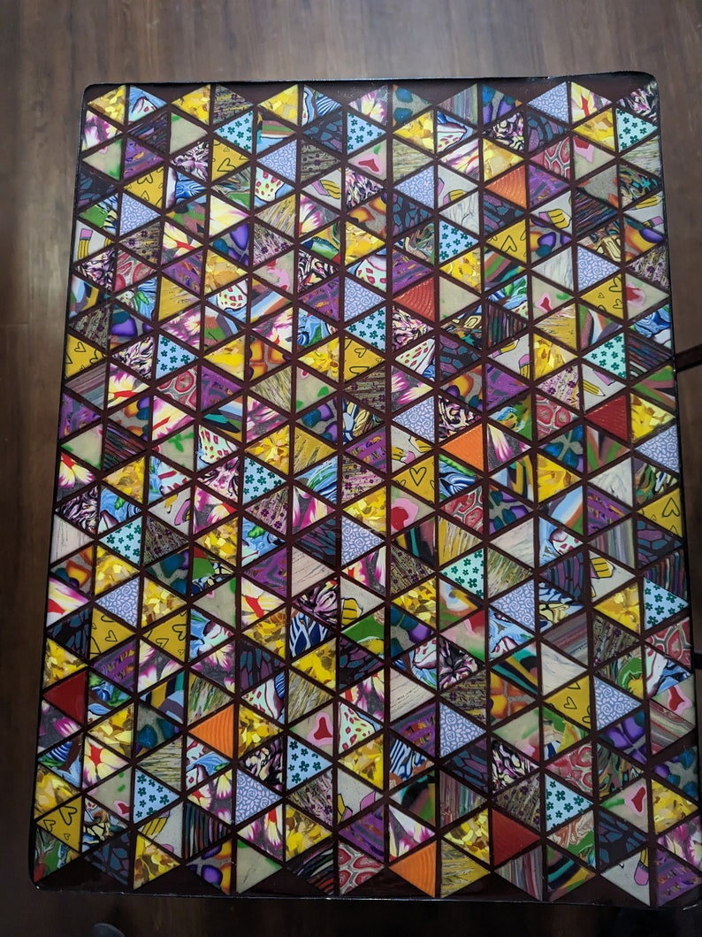May include: A table top with a geometric pattern of colorful triangles. The triangles are made of different fabrics and patterns, creating a vibrant and eclectic design.
