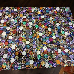 May include: A table top covered in a colorful hexagonal mosaic tile pattern. The tiles are made of various materials and have different patterns and colors, including purple, blue, green, yellow, red, and black.