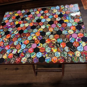 May include: A small, wooden table with a colorful, hexagonal mosaic tabletop. The mosaic is made of various fabrics and patterns, creating a vibrant and eclectic design.