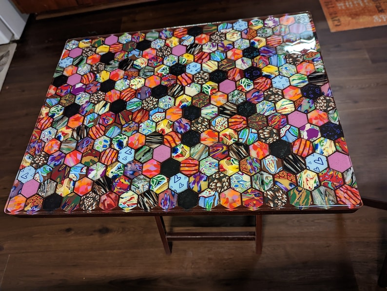 May include: A small, wooden table with a colorful, hexagonal mosaic tabletop. The mosaic is made of various fabrics and patterns, creating a vibrant and eclectic design.