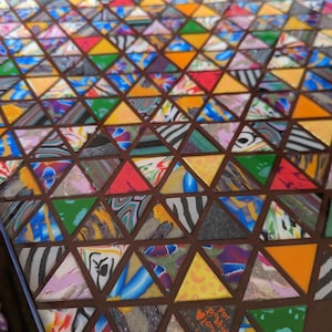 May include: A colorful mosaic table top with a geometric pattern of triangles. The table top is made of various materials, including wood, glass, and resin. The table top is decorated with a heart and the words "For Bobbie Love!" in orange.