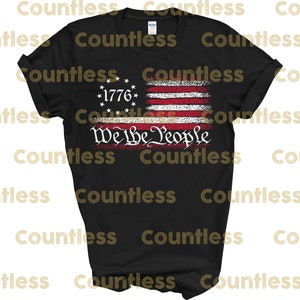 May include: Black t-shirt featuring a distressed American flag design with the text "We the People" in white. The flag has 13 red and white stripes and 13 white stars in a blue circle with the year "1776" in the centre.