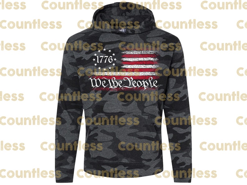May include: A black and grey camouflage hoodie with a distressed American flag design and the text "We The People" printed on the front. The flag is red, white and blue with a gold star in the top left corner. The text "1776" is printed above the flag.