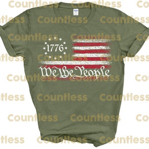 May include: A green t-shirt featuring a distressed American flag design with the text "We the People" and "1776" printed on it.