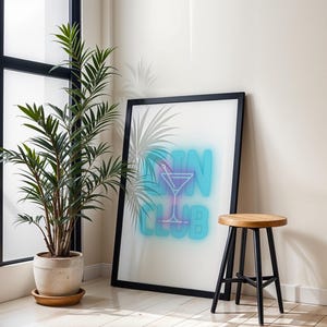 May include: A framed print with the words "GIN CLUB" in blue neon lettering, featuring a cocktail glass illustration. A wooden stool with black legs stands nearby. A potted plant sits next to a window.