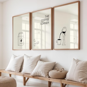 Op de afbeelding: Drie ingelijste spiegels met houten frames hangen boven een houten bank met kussens. De spiegels tonen zwart-wit illustraties van koffie gerelateerde afbeeldingen, waaronder een pak, bonen en een persoon die koffie in een kopje giet. De tekst "THE COFFEE CORNER" wordt ook weergegeven.