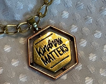 Necklace with pendant of mixed metals saying Kindness Matters hung on 18 inch chain of twisted cable brass