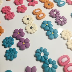 May include: Assortment of colorful polymer clay earrings featuring various flower designs, including blue, purple, pink, white, and orange. The earrings are handmade and unique.