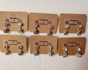 May include: Six pairs of dangle earrings with a small purse charm and a Hello Kitty-style cat charm. The earrings are on small cards with the text "Hothandbags & accessories".