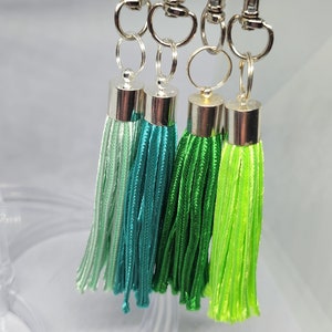 May include: Four green tassel keychains with silver clasps and rings. The tassels are different shades of green, from light green to dark green. The numbers 14, 21, 12, and 13 are printed below the tassels.