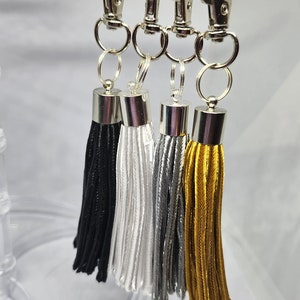 May include: Four keychains with silver clasps and tassels. The tassels are black, white, silver, and gold.