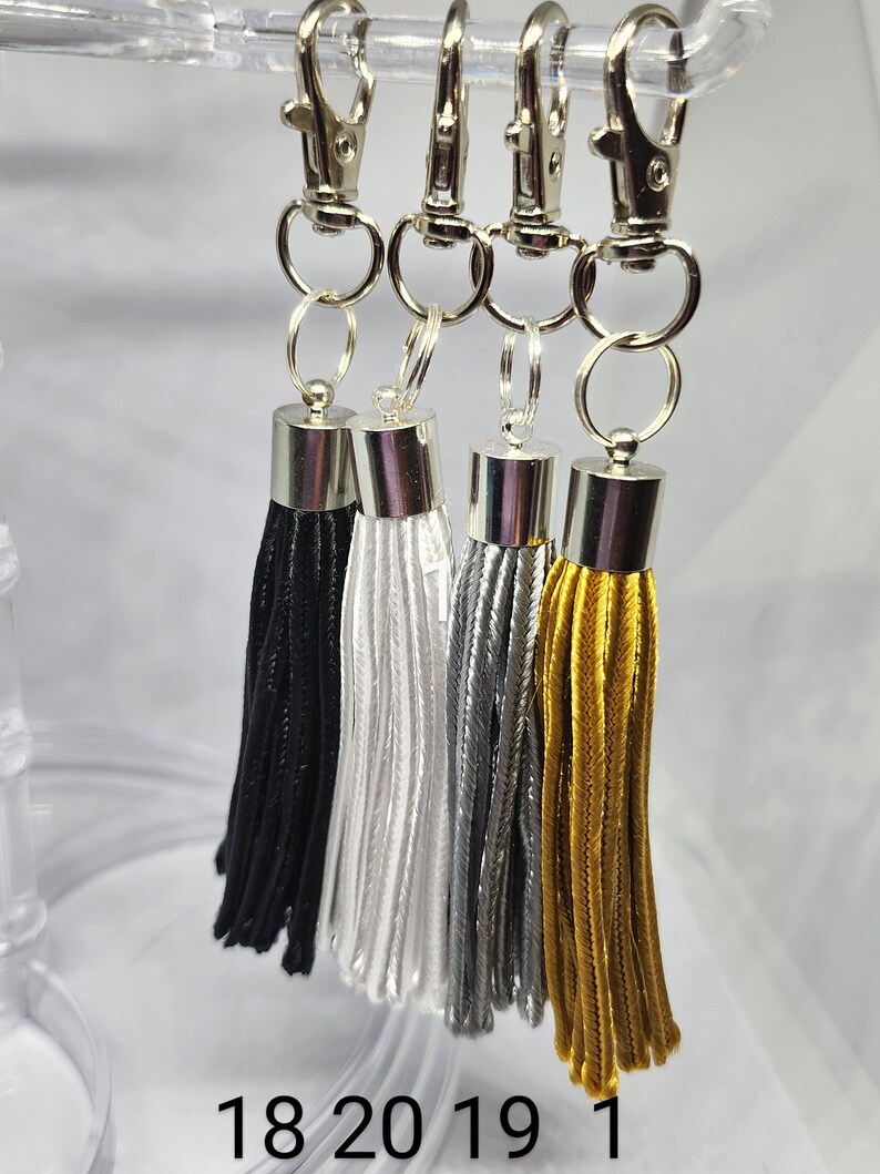 May include: Four keychains with silver clasps and tassels. The tassels are black, white, silver, and gold.