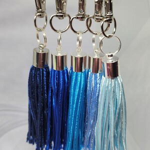 May include: Five blue and white tassel keychains with silver metal rings and clips. The tassels are arranged in a gradient from dark blue to light blue. The numbers 15, 16, 17, 27, and 28 are printed below the tassels.