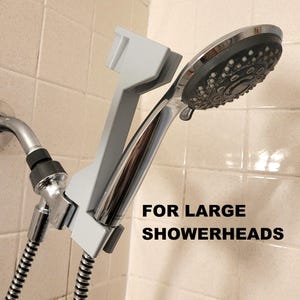 May include: A grey showerhead holder with the text "FOR LARGE SHOWERHEADS" is attached to a chrome shower arm and hose. The showerhead is silver and black.