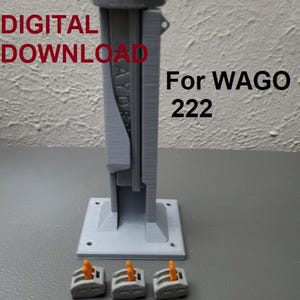 Puede incluir: Un conector de plástico gris impreso en 3D para bloques de terminales WAGO 222. El conector tiene una ranura para el bloque de terminales y una base con cuatro agujeros para montaje. Se muestran tres bloques de terminales WAGO 222 naranjas debajo del conector.
