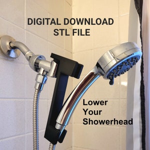 Könnte beinhalten: Ein schwarzer 3D-gedruckter Duschkopfhalter, der an einem Duscharm befestigt ist. Der Halter ist so konzipiert, dass er den Duschkopf absenkt. Der Text "Lower Your Showerhead" ist auf dem Bild zu sehen. Der Bildtext lautet außerdem "DIGITAL DOWNLOAD STL FILE".