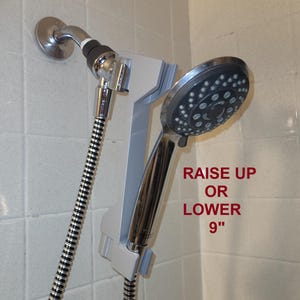 May include: A white shower head holder with a silver shower head attached. The holder allows you to raise or lower the shower head 9 inches.