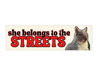 May include: A red and black sticker with the text "she belongs to the STREETS" and a picture of a grey squirrel.