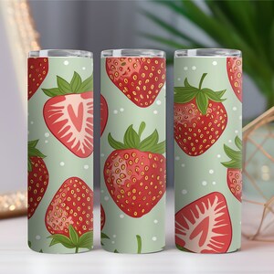 May include: Three cylindrical tumblers with a repeating pattern of red strawberries on a light green background. The strawberries have green leaves and white polka dots are scattered across the surface. One tumbler shows a strawberry cut in half.