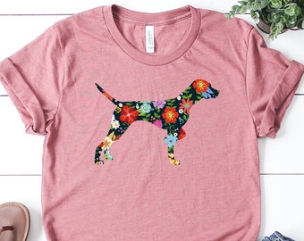 Peut inclure: Un t-shirt mauve avec une silhouette de chien imprimée de fleurs. Le t-shirt est associé à un jean bleu et des sandales marrons.
