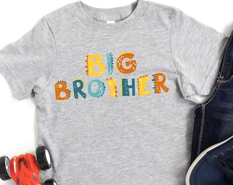 May include: A gray short-sleeved t-shirt with the words "BIG BROTHER" in colorful letters. The shirt is paired with blue jeans and blue sneakers.