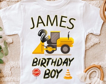 May include: White t-shirt with a yellow construction vehicle graphic, the number 2, and the text "JAMES BIRTHDAY BOY".