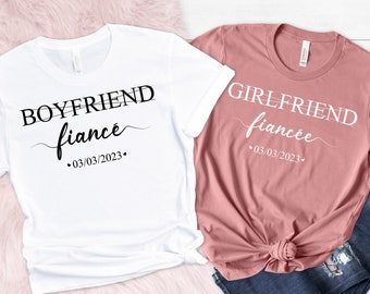May include: Two white t-shirts with black text. The left shirt says "Boyfriend fiance" with the date "03/03/2023". The right shirt says "Girlfriend fiancee" with the date "03/03/2023".