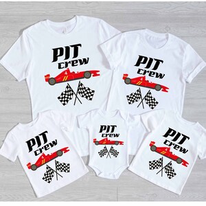 Pode incluir: Quatro camisetas brancas com um carro de corrida vermelho e bandeiras xadrez. As camisetas dizem "PIT CREW" em letras pretas.