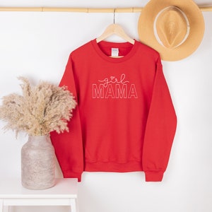 Peut inclure: Sweat-shirt rouge avec le texte "girl MAMA" en lettres blanches soulign&eacute;es. Le texte comprend un petit symbole de c&oelig;ur au-dessus du mot "girl".