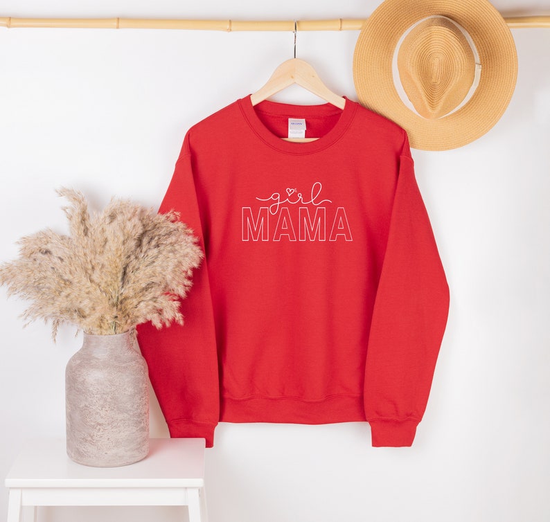 Peut inclure: Sweat-shirt rouge avec le texte "girl MAMA" en lettres blanches soulign&eacute;es. Le texte comprend un petit symbole de c&oelig;ur au-dessus du mot "girl".