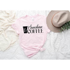 May include: Pink t-shirt with a black graphic of a coffee cup and the text "Sunshine & COFFEE".