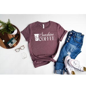 May include: A maroon t-shirt with white text that reads "Sunshine & COFFEE" and a white graphic of a coffee cup.