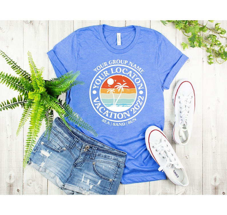 May include: A blue t-shirt with a white circle graphic that says "Your Group Name Your Location Vacation 2022 Sea | Sand | Sun". The graphic features a sunset with palm trees and a beach.