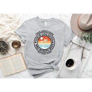 May include: Gray t-shirt with a black circle graphic featuring a sunset, palm trees, and the text "Your Group Name Your Location Vacation 2022 Sea | Sand | Stars".