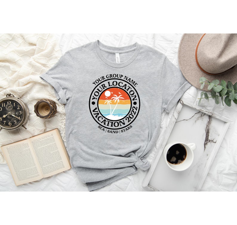May include: Gray t-shirt with a black circle graphic featuring a sunset, palm trees, and the text "Your Group Name Your Location Vacation 2022 Sea | Sand | Stars".