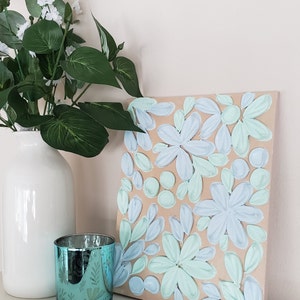 May include: A canvas painting with a textured, raised floral design. The flowers are painted in shades of light blue and green on a beige background.