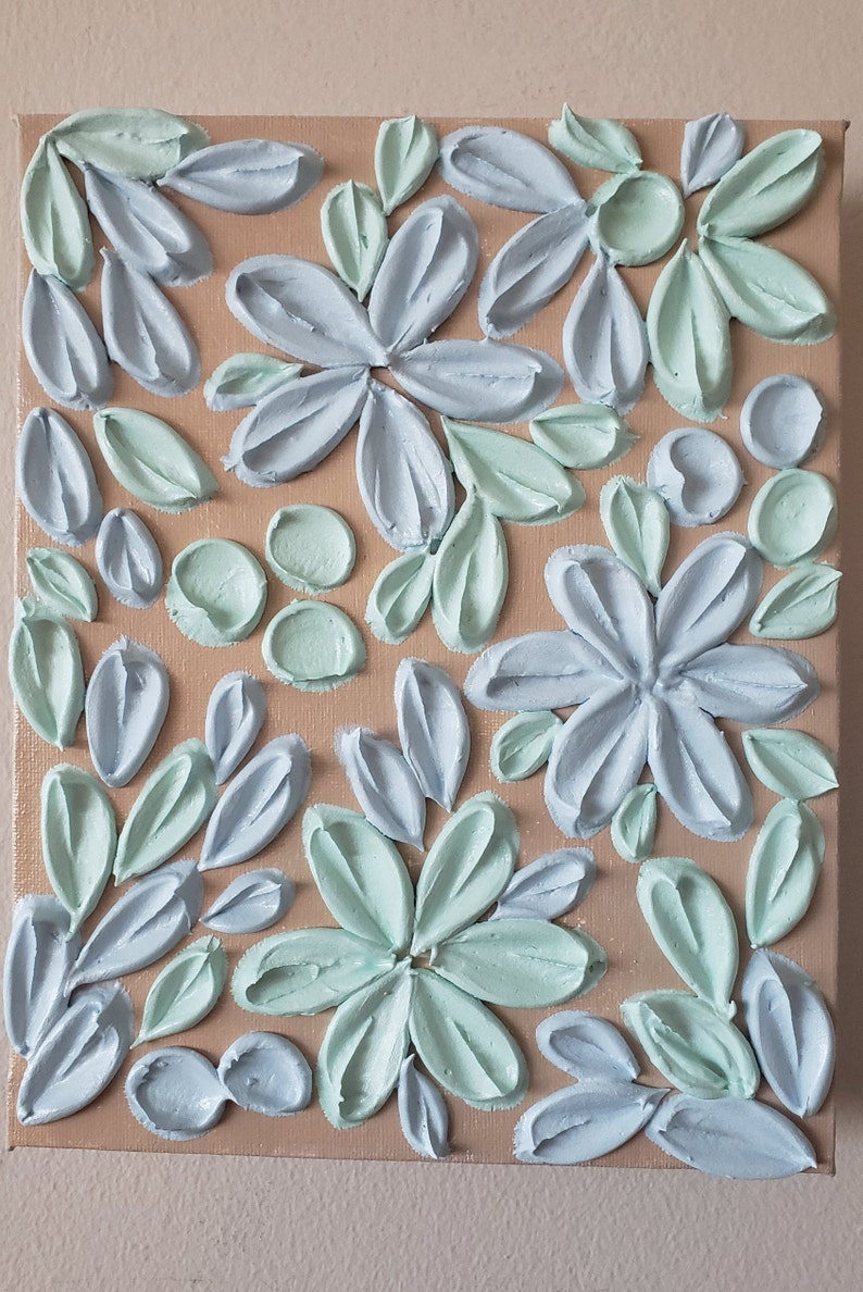 May include: A close-up of a canvas painting with a textured, raised floral design. The flowers are painted in shades of light blue and light green on a beige background.