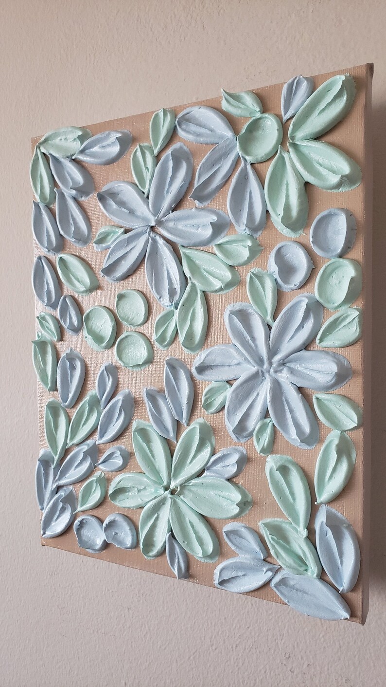 May include: A square canvas painting with a textured, raised paint design. The painting features a floral pattern with blue and green flowers and leaves.