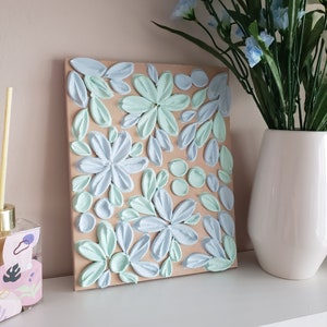 May include: A light blue and mint green floral painting on a canvas with a brown background. The painting is made with textured paint and has a 3D effect.