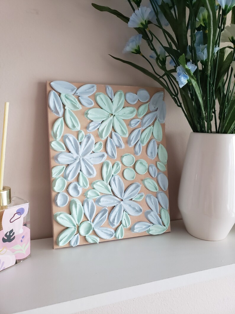 May include: A light blue and mint green floral painting on a canvas with a brown background. The painting is made with textured paint and has a 3D effect.